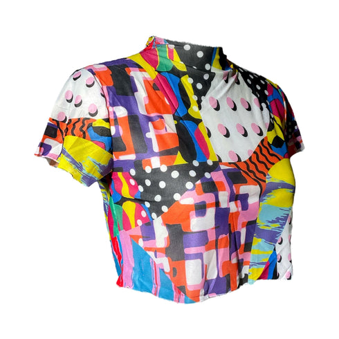 A colorful 90s-style mesh crop top featuring a maximalist abstract pattern. This see-through shirt has a high mock neck, short sleeves, and a vibrant, retro design with geometric shapes, color blocking, and polka dots in bold shades of pink, yellow, blue, and orange. The Y2K-inspired top is a statement piece of festival clothing, perfect for a rave outfit or alternative, dopamine-dressing-inspired streetwear looks.